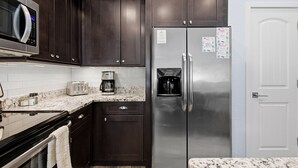 A compact kitchen with dark wood cabinets, a stainless steel refrigerator, a microwave, a toaster, and a coffee maker. - Terrapin Station (Ormond Beach)