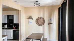 Una cocina con armarios blancos, una encimera negra y una olla roja. En primer plano, una mesa de madera con bancos.