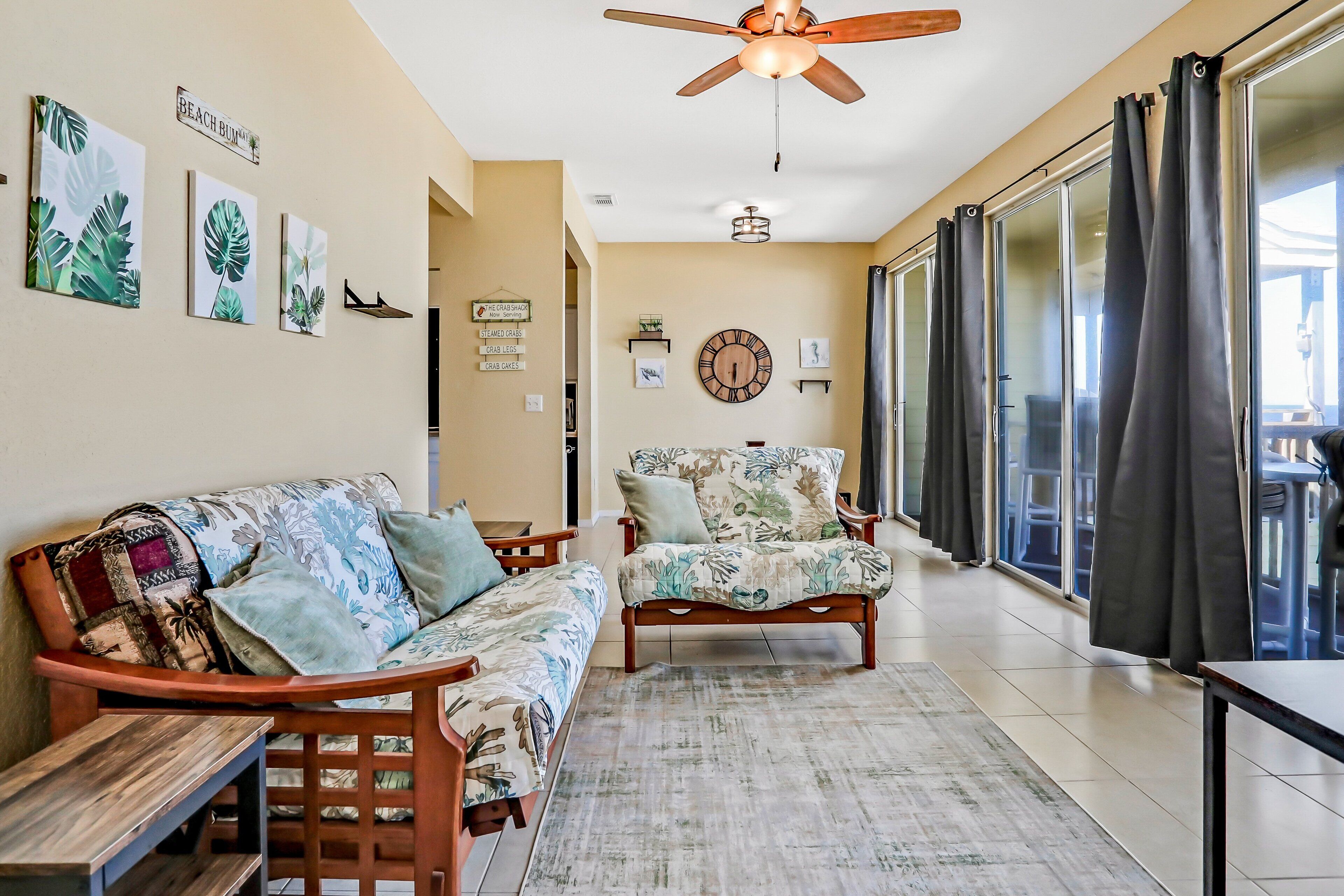 A living room with a ceiling fan, a sofa, a chair, and a large window with curtains.