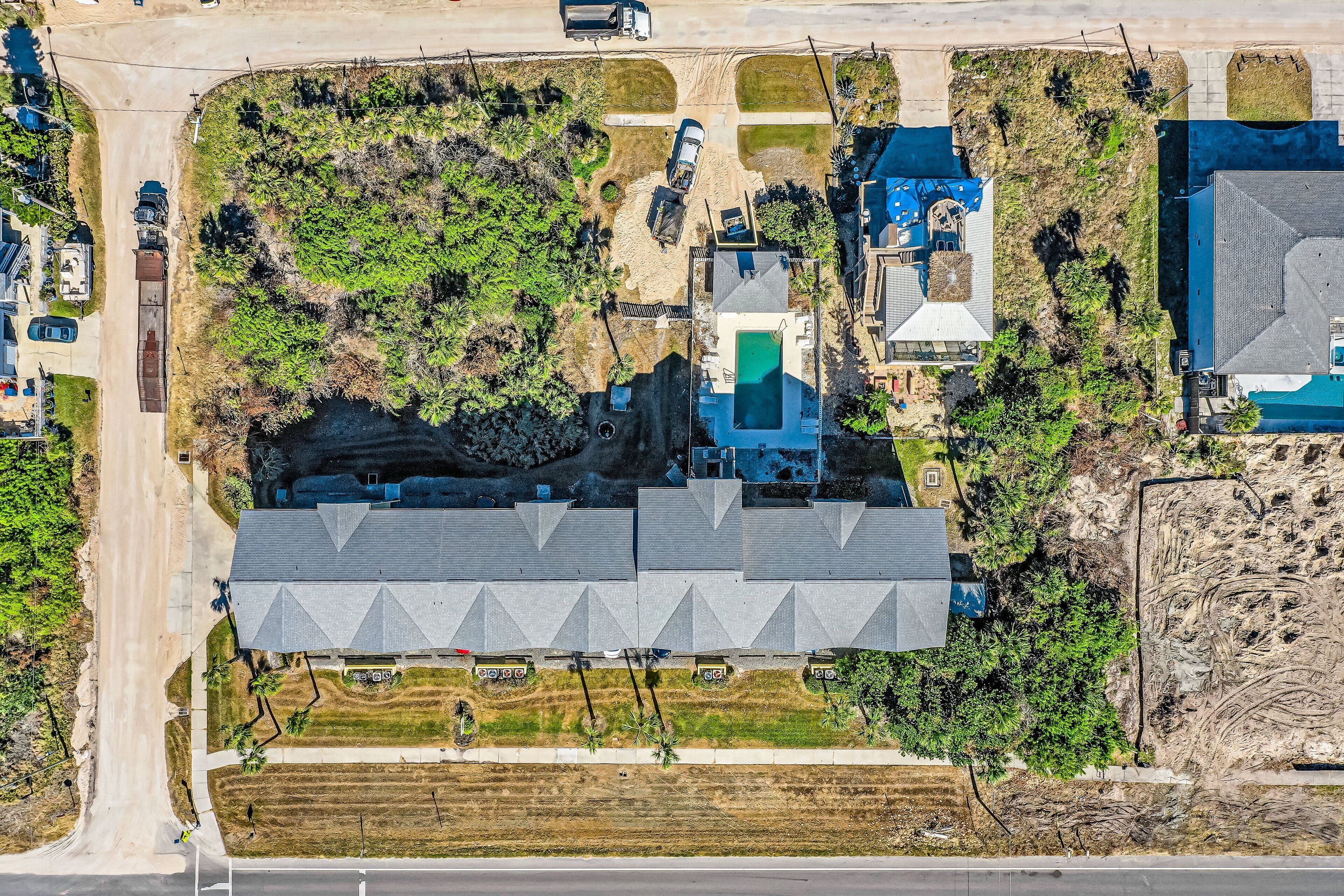 An aerial view of a residential area with a large house featuring a unique triangular roof design, a swimming pool, and a well-maintained lawn.