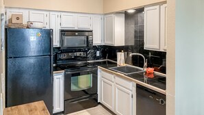 Una cocina con armarios blancos, un refrigerador negro, un microondas, una estufa y un lavamanos.
