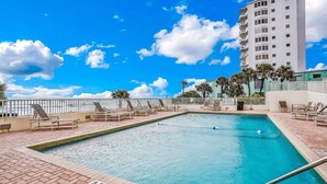 A swimming pool with lounge chairs and a high-rise building in the background. - Seawinds 204 - Sea Wind Enjoyment (Ormond Beach)