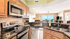 A kitchen with stainless steel appliances, wooden cabinets, and a black granite countertop. - Seawinds 204 - Sea Wind Enjoyment (Ormond Beach)