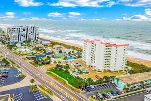 A coastal hotel with multiple floors, a parking lot, and a view of the beach and ocean.