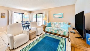 A living room with a sofa, two armchairs, a TV, and a dining area with a table and chairs. - NSB Seaward D-101 (New Smyrna Beach)