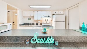 A kitchen with white cabinets, a microwave, a stove, and a refrigerator. - NSB Seaward D-101 (New Smyrna Beach)