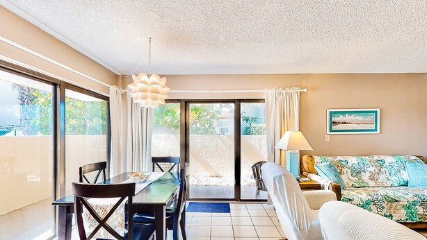 A well-lit room with a dining table, chairs, a sofa, and a large window. - NSB Seaward D-101 (New Smyrna Beach)