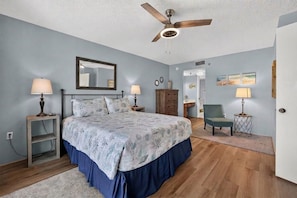 A bedroom with a bed, a ceiling fan, a dresser, a chair, and a nightstand. - Ormondy A6 - Ocean Shores Getaway (Ormond Beach)