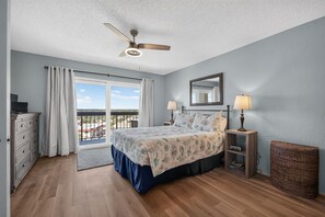 A bedroom with a bed, two bedside lamps, a ceiling fan, a dresser, a window with curtains, and a view of the outside. - Ormondy A6 - Ocean Shores Getaway (Ormond Beach)