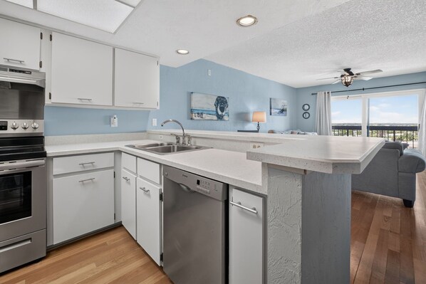 A modern kitchen with a dishwasher, a built-in oven, and a large island with seating. - Ormondy A6 - Ocean Shores Getaway (Ormond Beach)