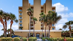 A multi-story hotel with a central tower, balconies, and palm trees in the foreground. - NSB Malibu Condos 804-malibu 804 (New Smyrna Beach)