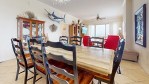 A dining room with a wooden table and chairs, a chandelier, decorative wall art, and a ceiling fan. - NSB Malibu Condos 804-malibu 804 (New Smyrna Beach)