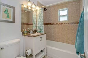 A bathroom with a toilet, sink, vanity, mirror, shower curtain, and a bathtub. - Bathing Suit Beach Bungalow (Ormond Beach)