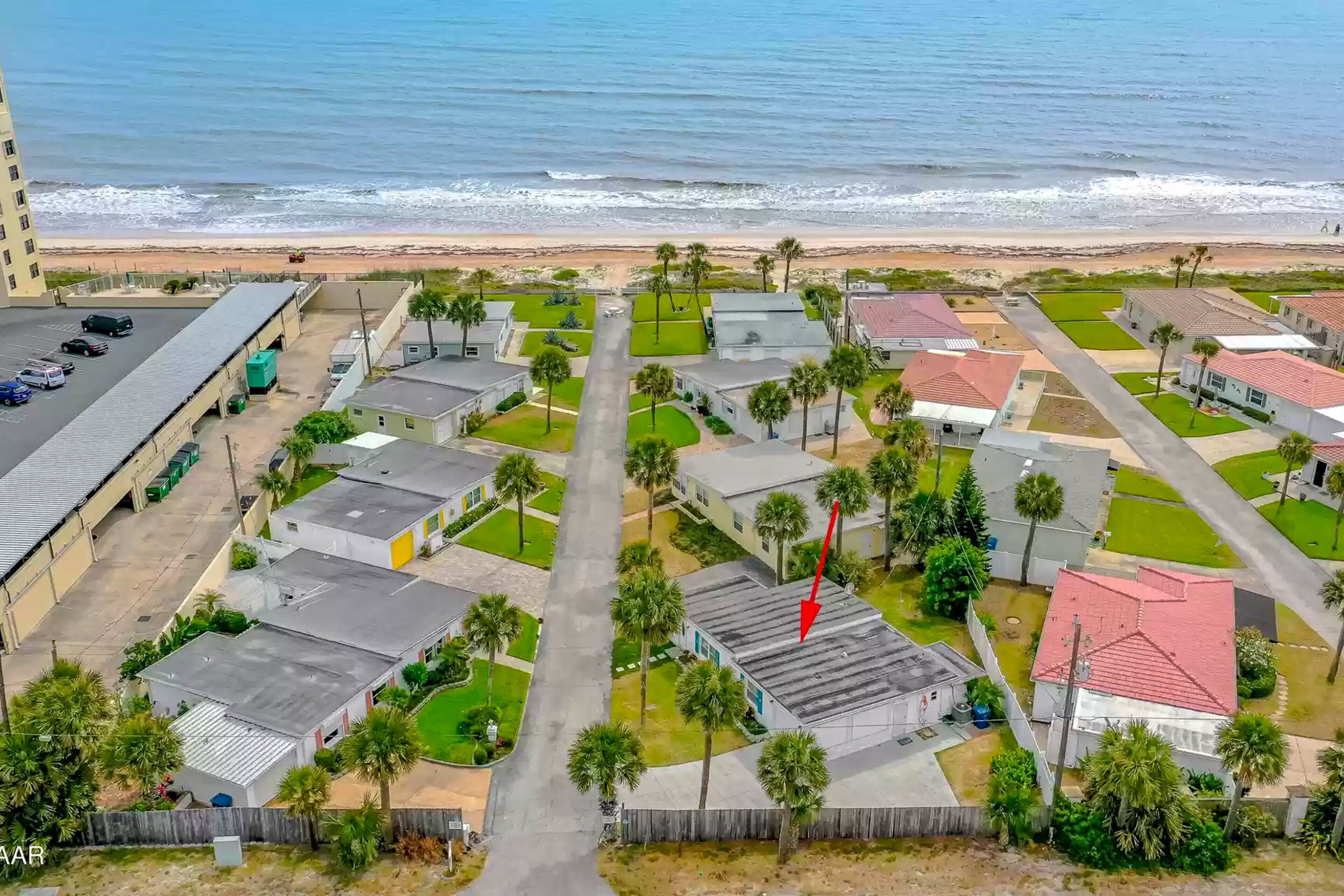 An aerial view of a coastal residential area with houses, a beach, and a parking lot.