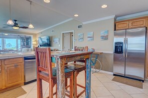 A kitchen with wooden cabinets, a stainless steel refrigerator, and a dining table with chairs. - Bathing Suit Beach Bungalow (Ormond Beach)