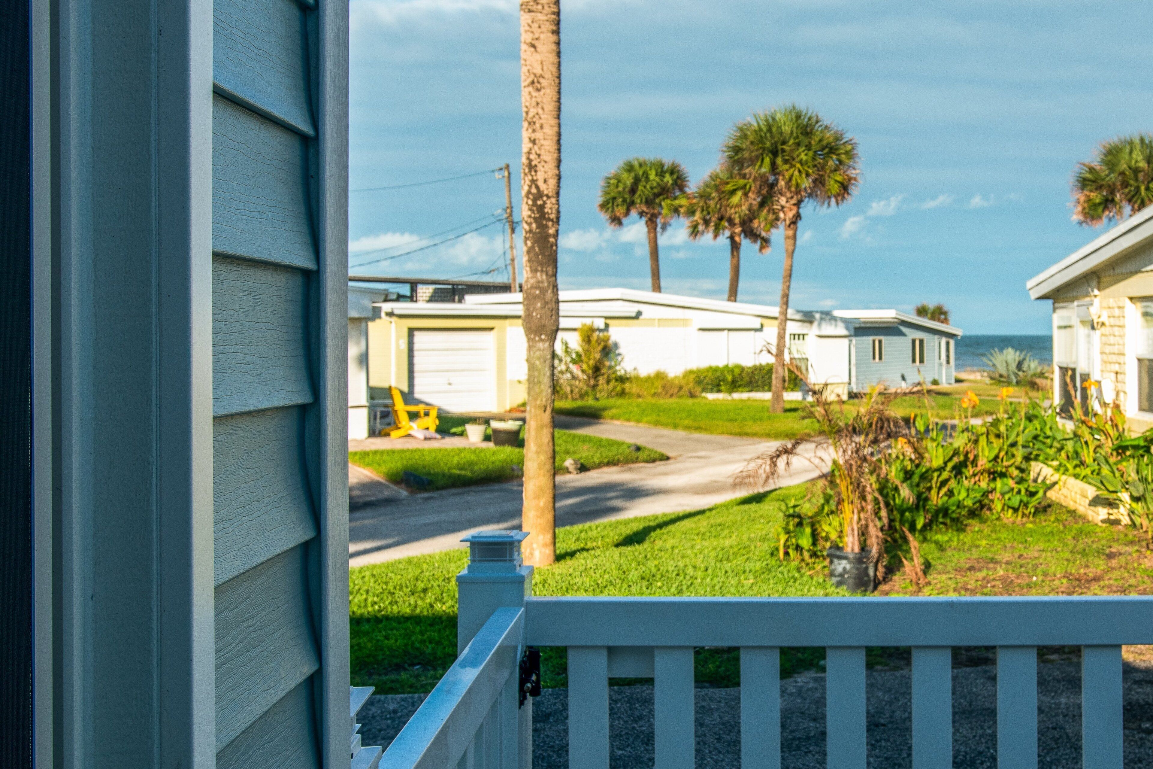 A view of a residential area with houses, a road, and a grassy area with palm trees.