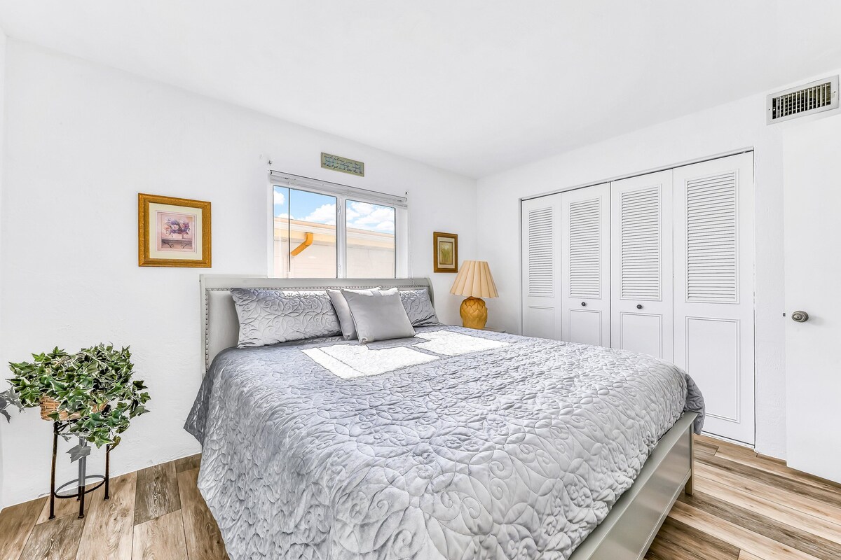 A bedroom with a large bed, a window, a plant, and a wardrobe.