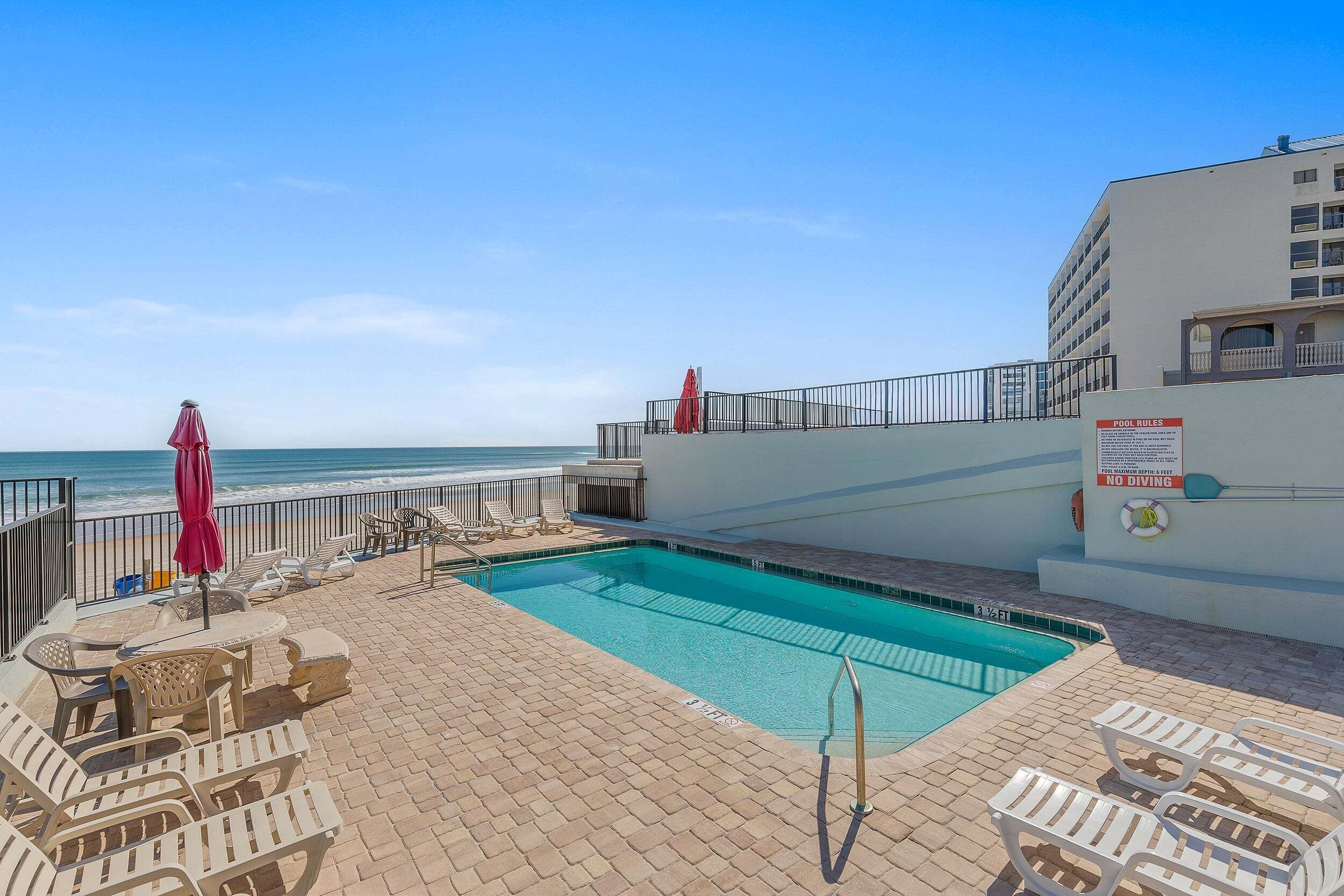 A pool area with lounge chairs and umbrellas, a lifebuoy, and a sign indicating no diving.