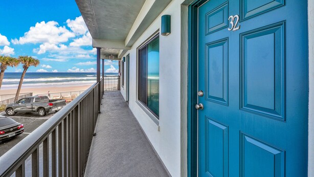 A balcony with a view of the beach, a blue door with the number 32, and a parked truck. - Daytona Atlantico 32 (Daytona Beach)