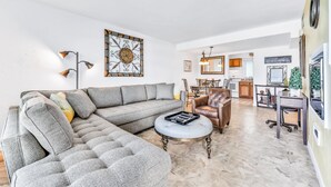 A modern living room with a sectional sofa, a round coffee table, and a dining area with a chair and table. - Daytona Atlantico 32 (Daytona Beach)