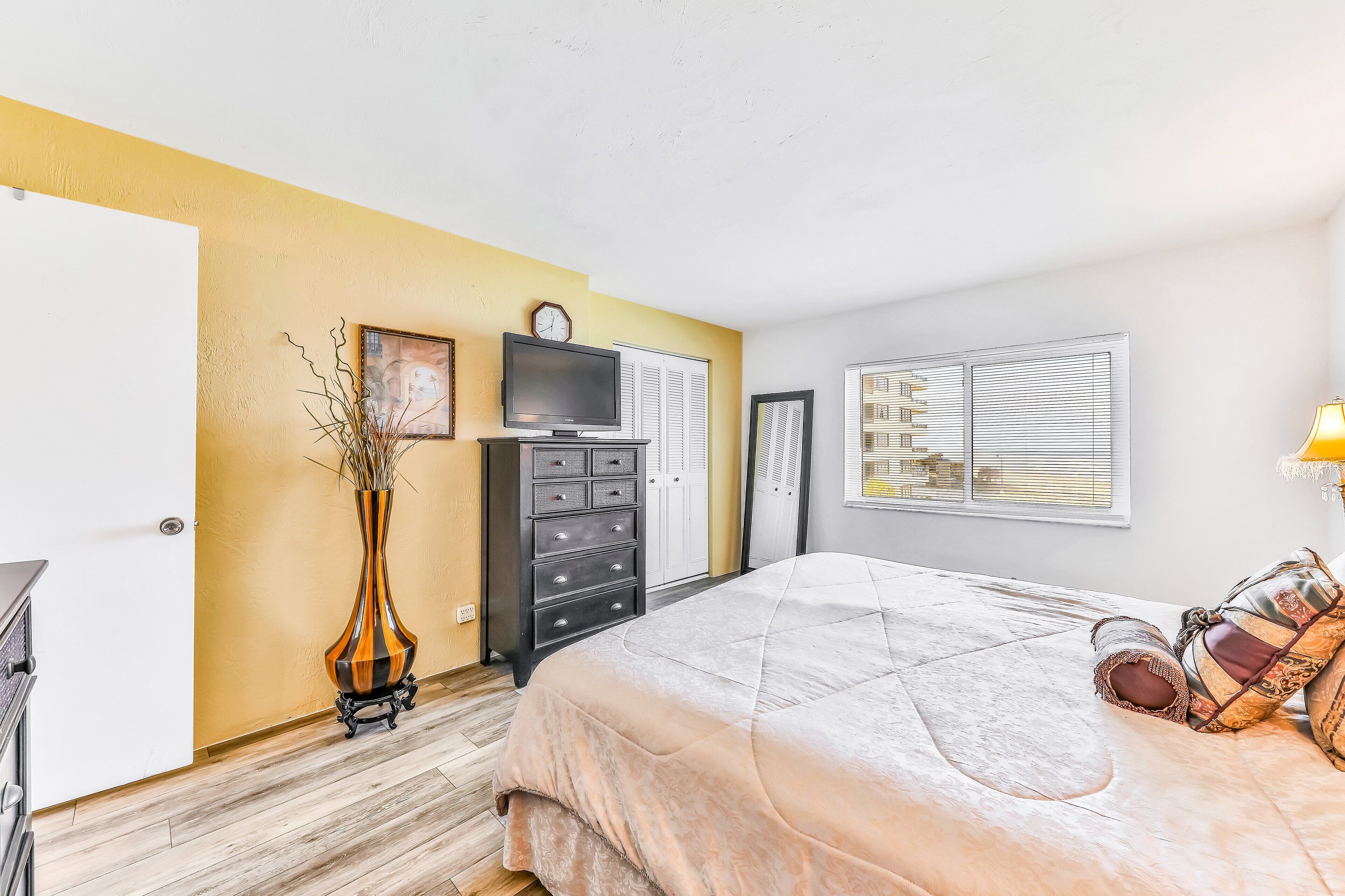 A bedroom with a bed, dresser, TV, and a window with blinds.