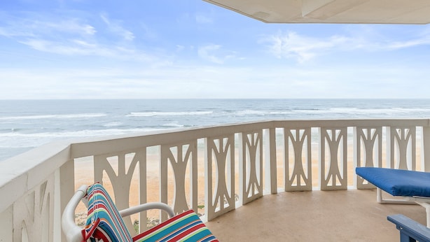Un balcon avec vue sur l’océan, une balustrade blanche et un fauteuil bleu avec coussin.