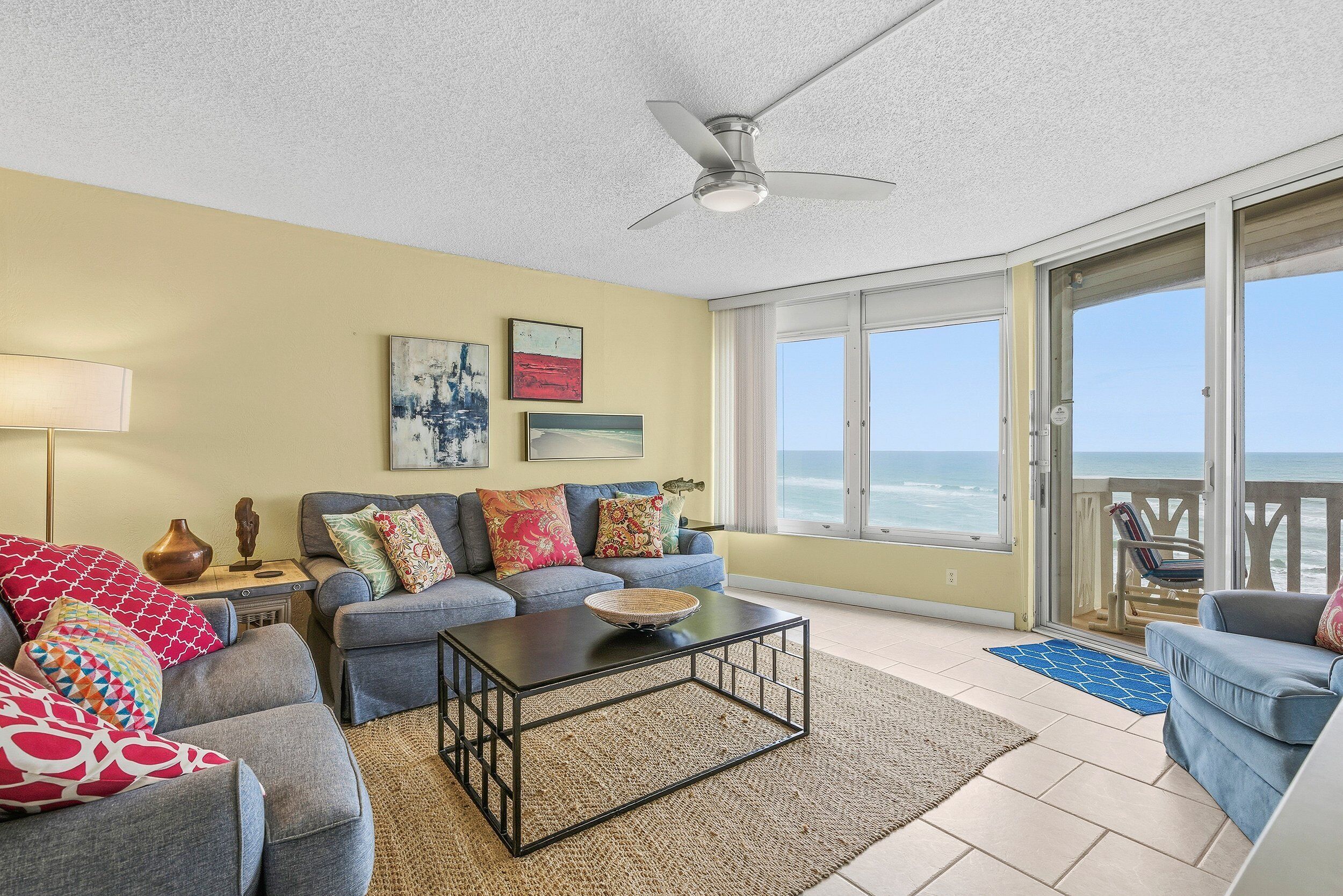 A living room with a sofa, coffee table, and a balcony with a view of the ocean.