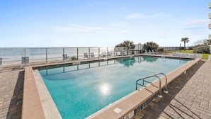 Une piscine rectangulaire à l’eau d’un bleu limpide, entourée d’une terrasse en briques et d’une rambarde en métal.
