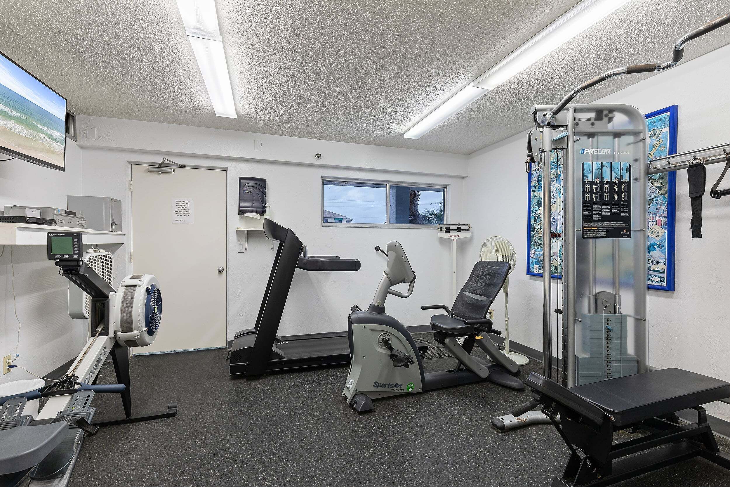 Ein Fitnessraum mit Cardiogeräten, einer Hantelbank und einem an der Wand befestigten Fernseher.