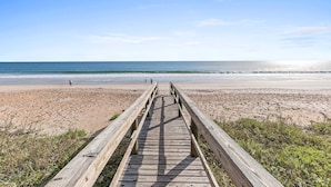 Une promenade en bois qui mène à une plage, sous un ciel dégagé.