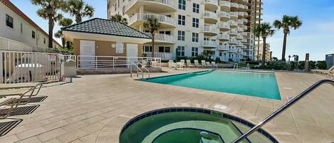 Un espace piscine comprenant un jacuzzi, des chaises longues et un bâtiment doté de balcons en arrière-plan.