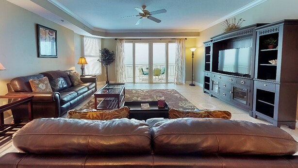 Una sala de estar con un sofá de cuero, una mesa de centro, un televisor y un balcón con vistas.