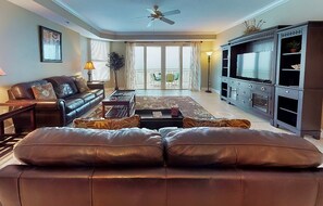 A living room with a leather sofa, a coffee table, a TV, and a balcony with a view. - Daytona Eleventh Heaven @ The St. Maarten (Daytona Beach Shores)