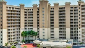 Un hotel de altura con varios balcones, un estacionamiento y un patio central con palmeras.