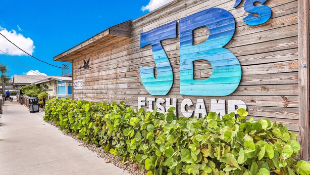 En vägg av trä med stora, blå bokstäver som bildar texten "JB's FISH CAMP".
