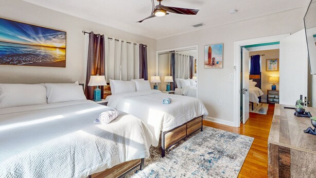 A hotel room with two beds, a ceiling fan, a large painting of a sunset, and a view into the adjacent room. - Daytona Beach Retreat (Daytona Beach)