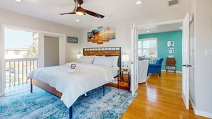 A bedroom with a bed, ceiling fan, artwork, and a view to the outside. - Daytona Beach Retreat (Daytona Beach)