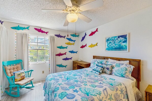 Quarto com cama, cadeira de balanço, ventoinha no teto e detalhes decorativos nas paredes.