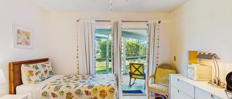 Um quarto com cama, poltrona, escrivaninha e ventilador de teto.