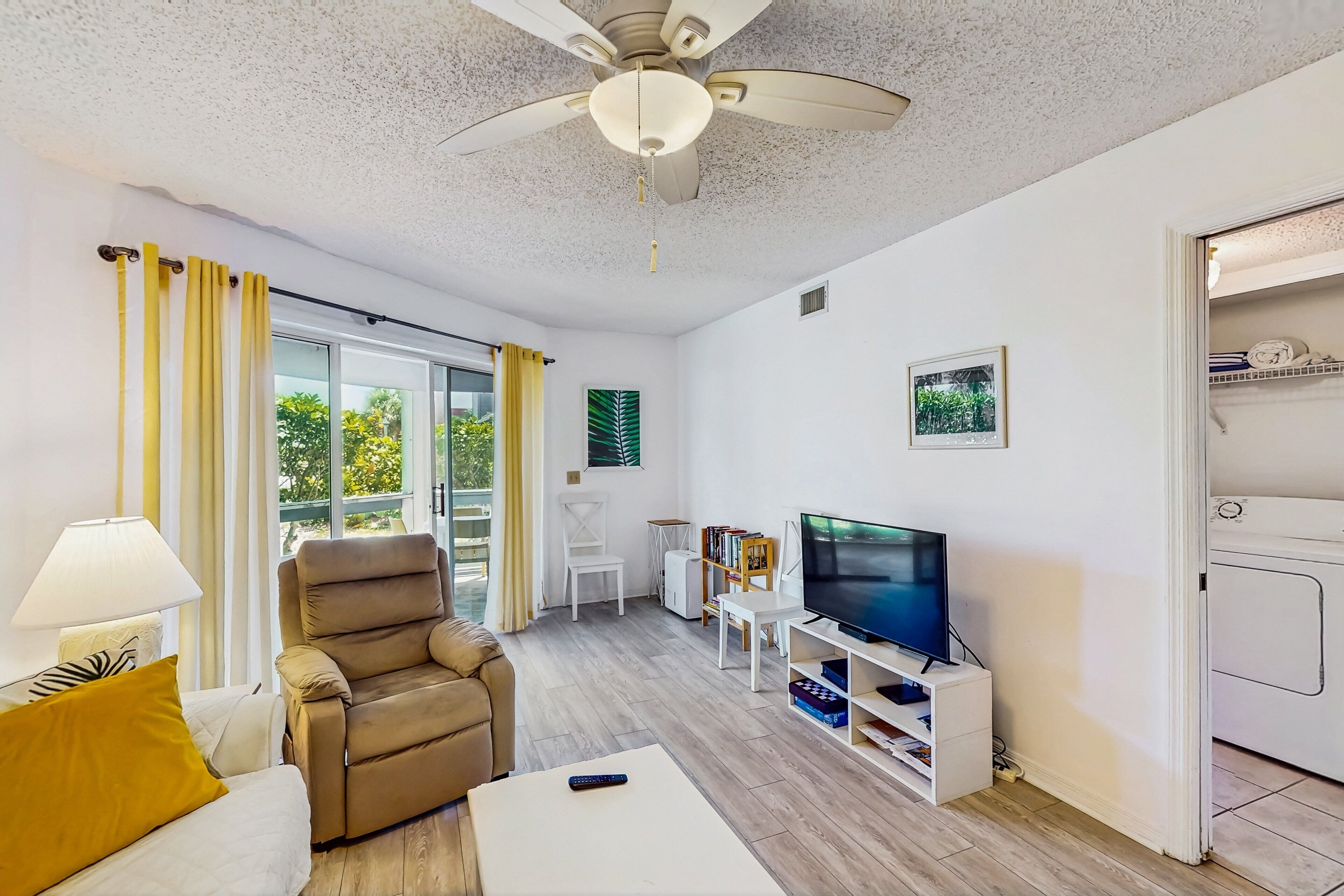 A modern living room with a ceiling fan, a sofa, a recliner, a TV, and a bookshelf.