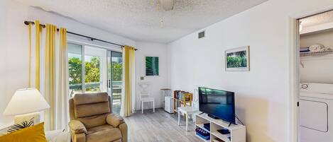 A modern living room with a ceiling fan, a sofa, a recliner, a TV, and a bookshelf.