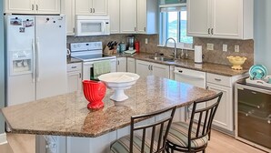Una cocina moderna con armarios blancos, encimeras de granito, horno empotrado y refrigerador.