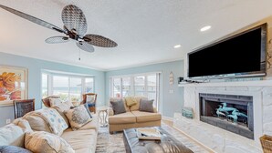 Un salón amplio con un sofá color beige, un reposapiés de cuero, una chimenea y un ventilador de techo.