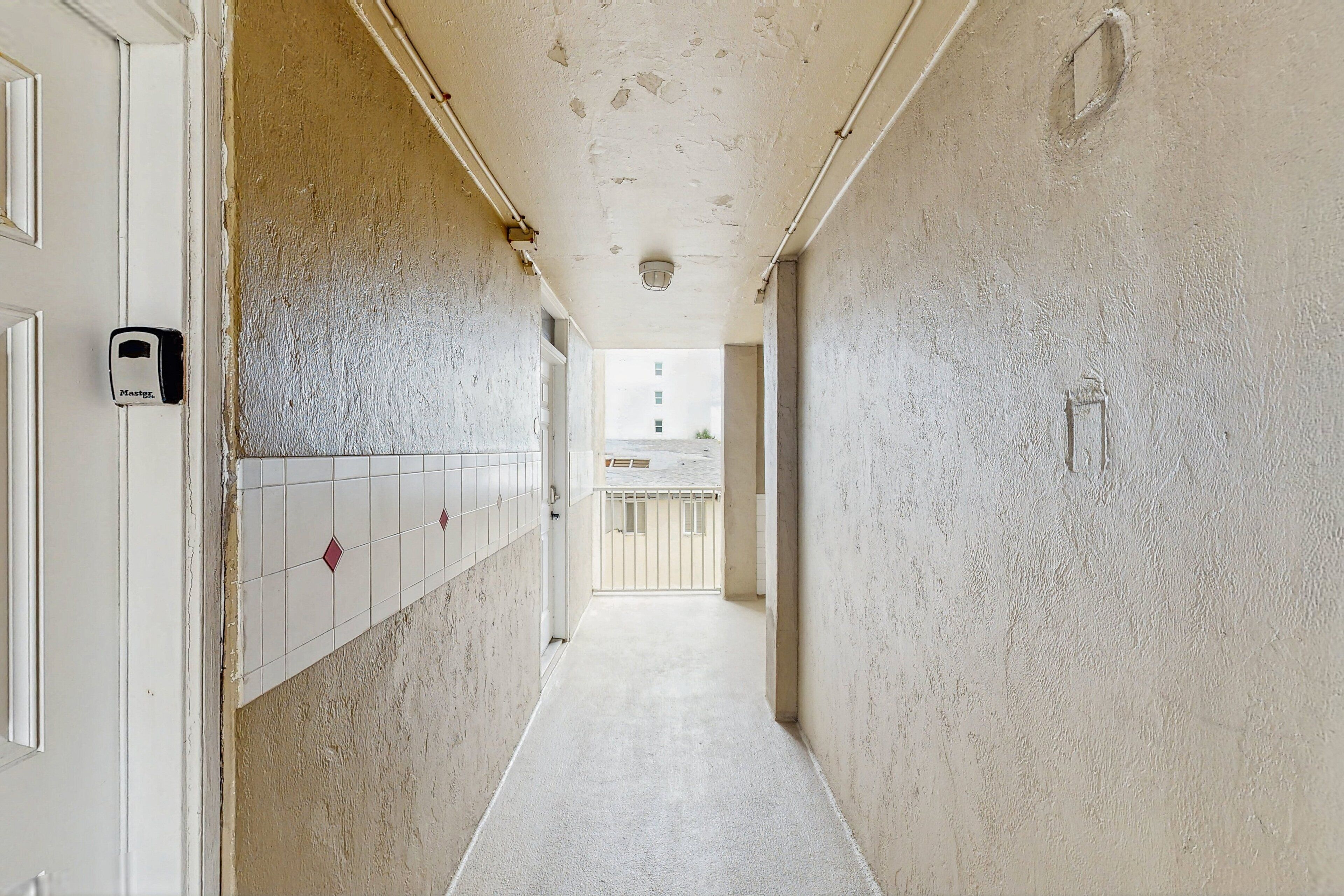 A narrow hallway with white tiled walls and a concrete floor.