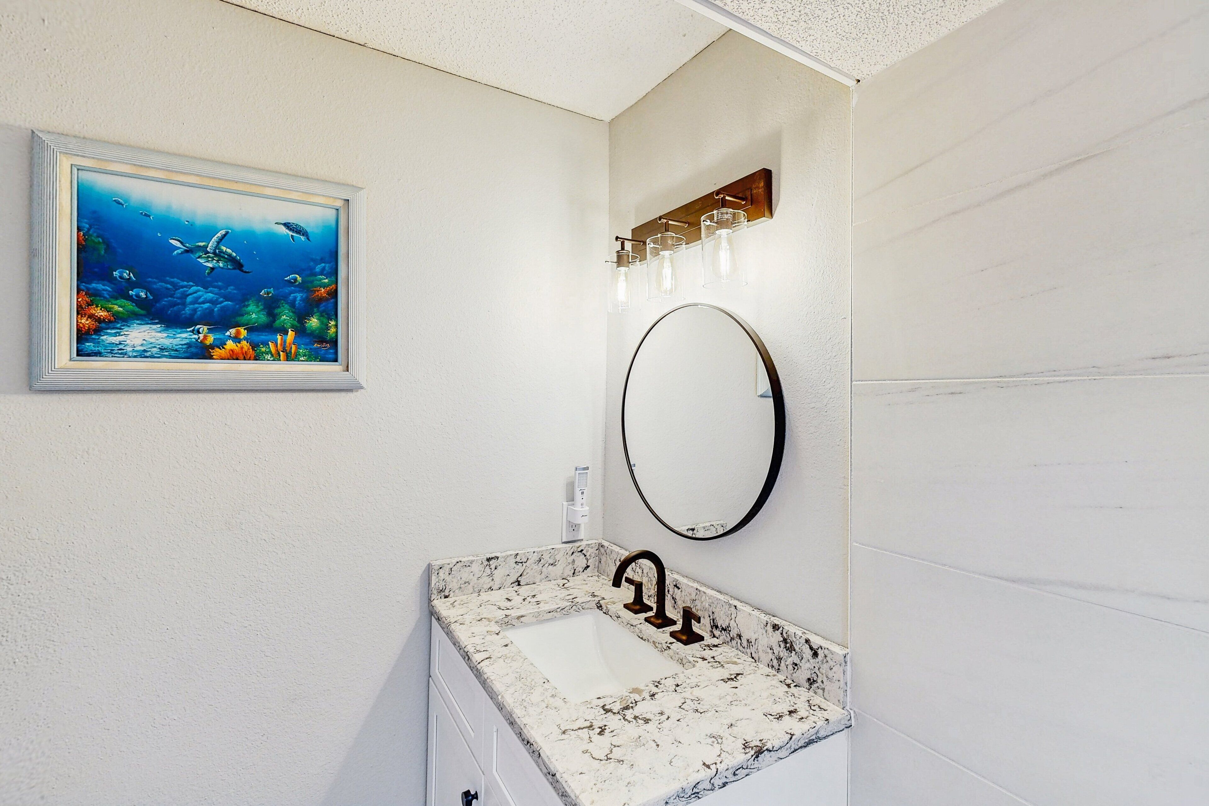 A bathroom with a white marble sink, a round mirror, and a framed painting of an underwater scene.