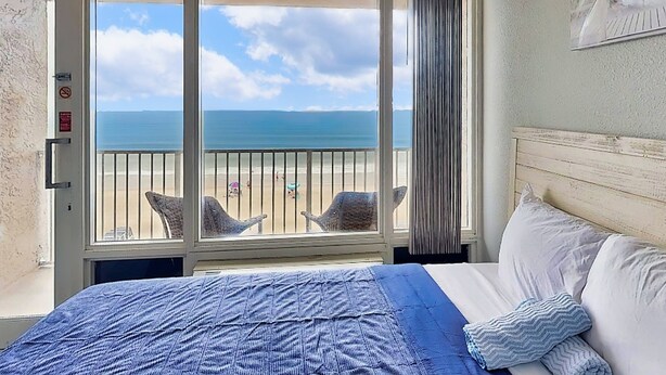 A hotel room with a bed, a view of the beach, and a balcony with chairs. - Daytona Pirates Cove 3270-salt Air Cove (Daytona Beach Shores)
