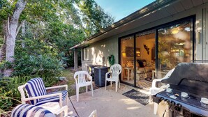 Un'area patio con mobili da esterno, un barbecue e una porta scorrevole che dà su un portico coperto.