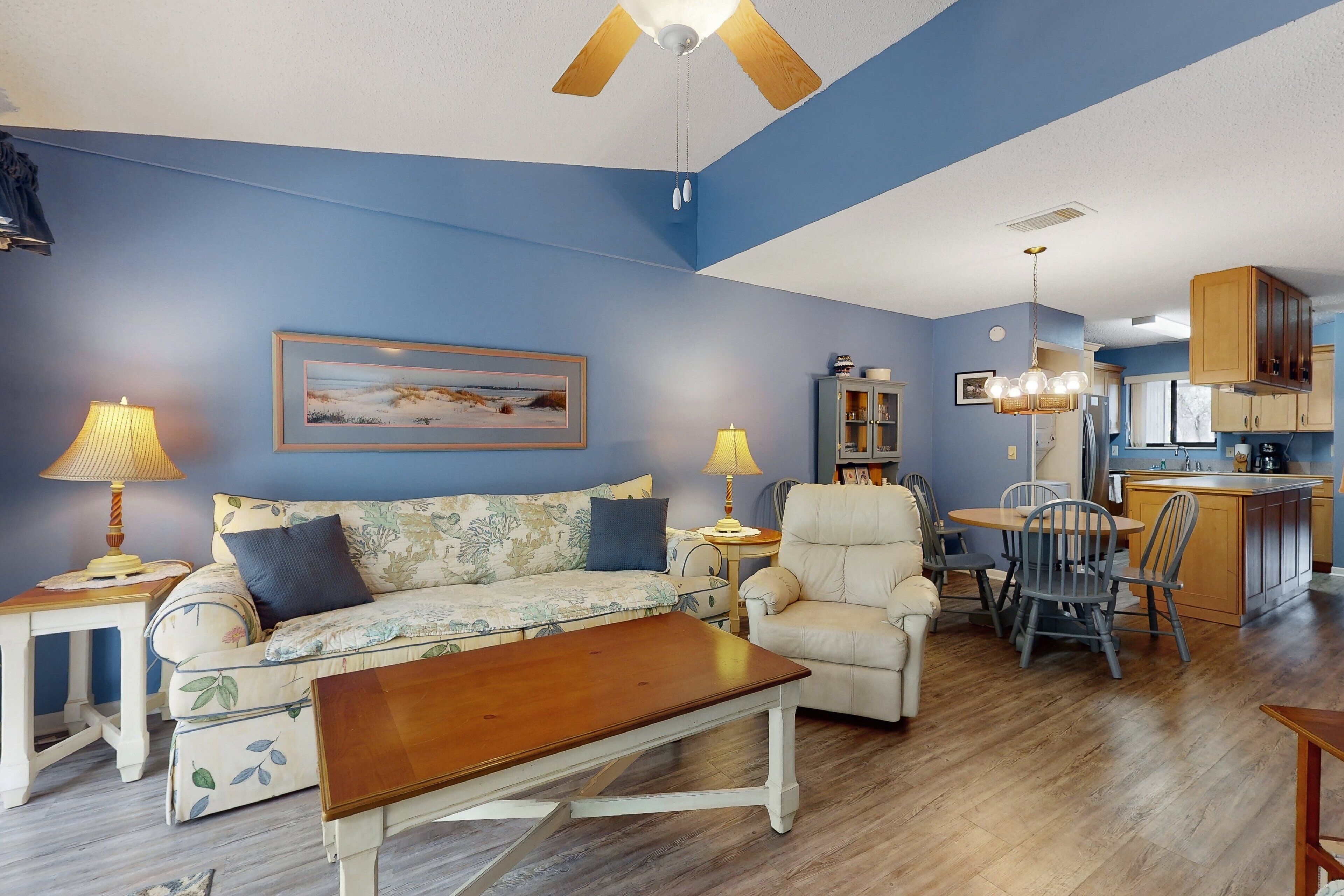 A living room with a sofa, armchair, and coffee table, a dining area with a table and chairs, and a kitchen with cabinets and a sink.