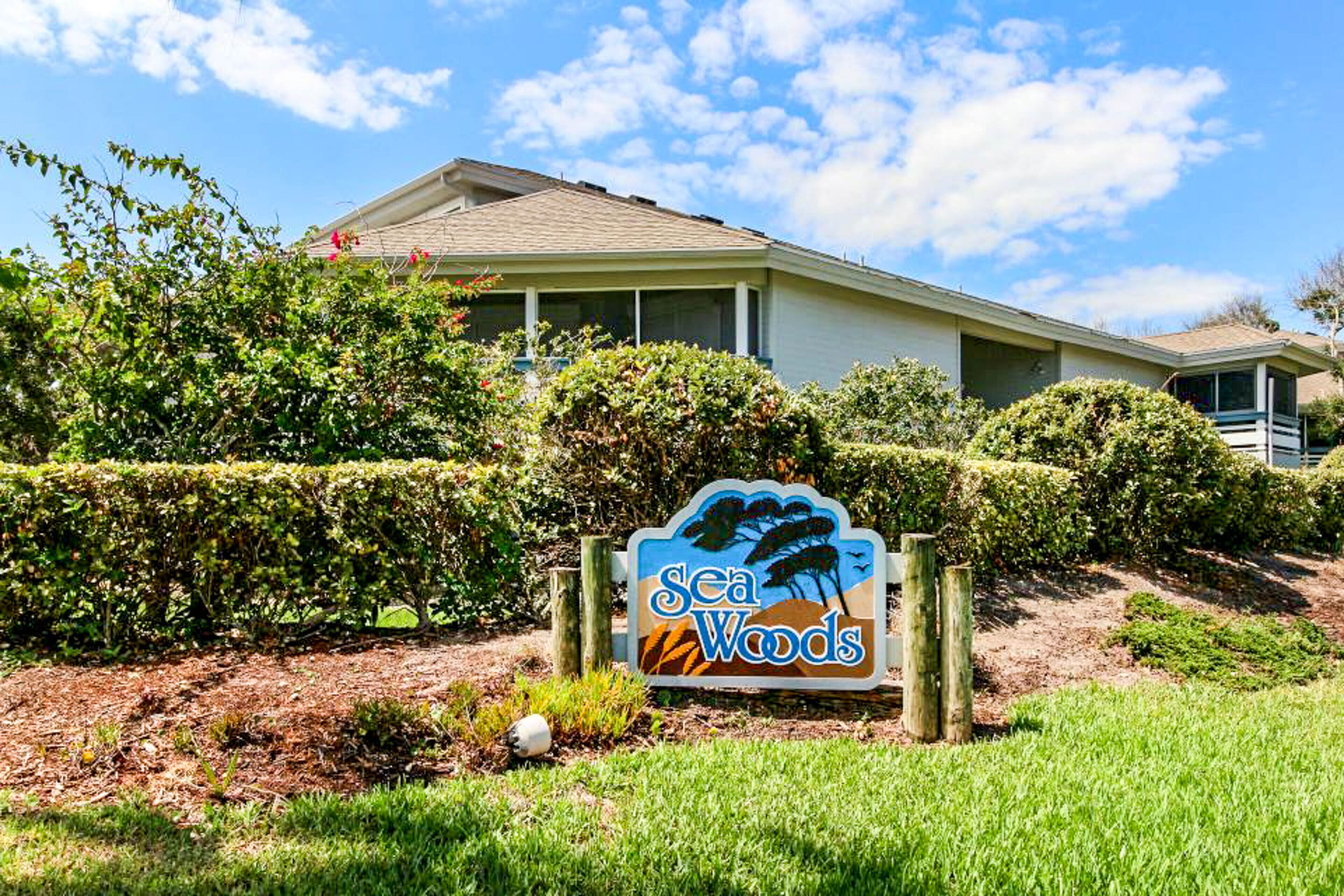 A sign for Sea Woods with a house in the background.