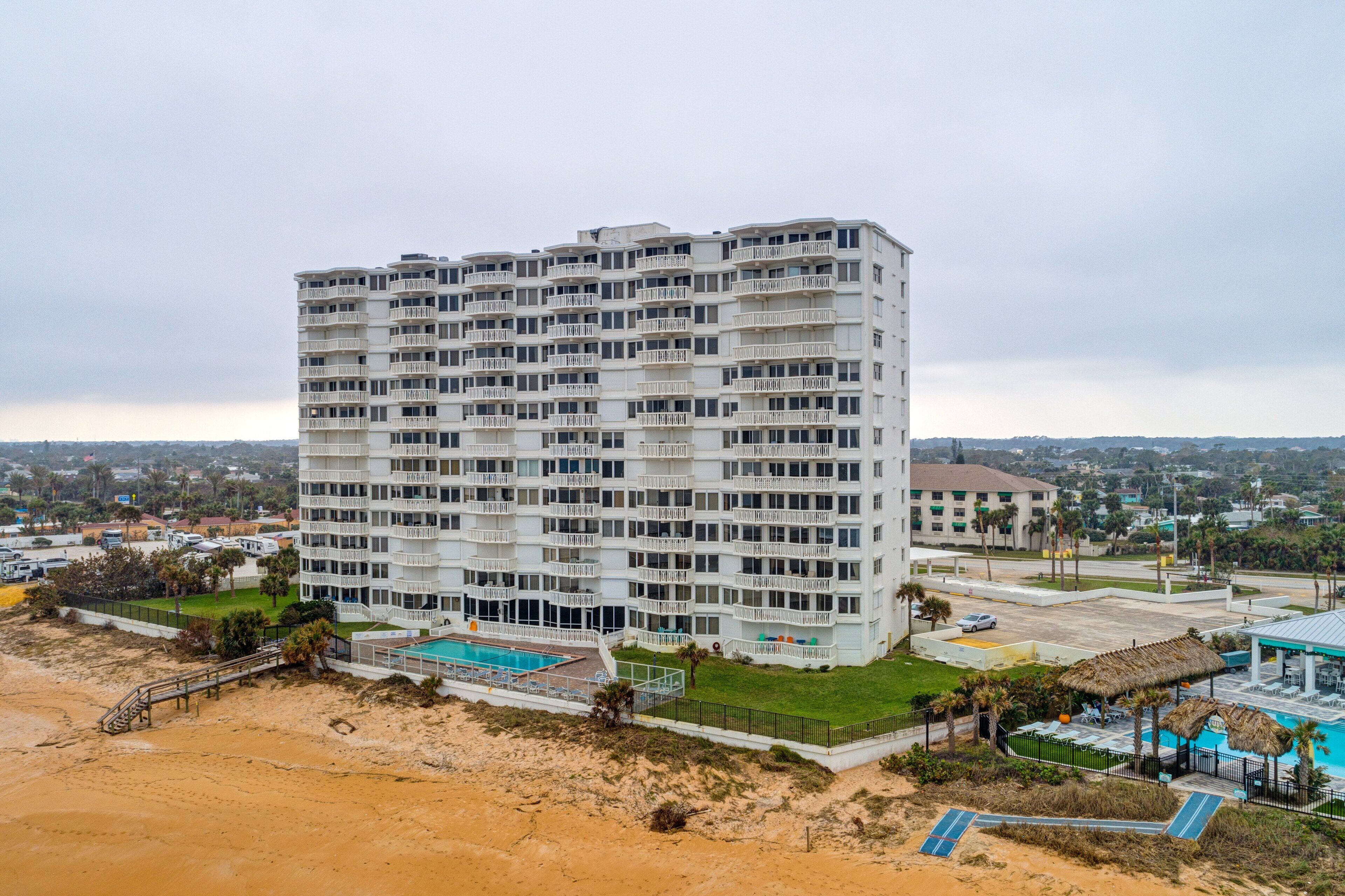 Um hotel com vários andares, varandas, piscina e área de praia.